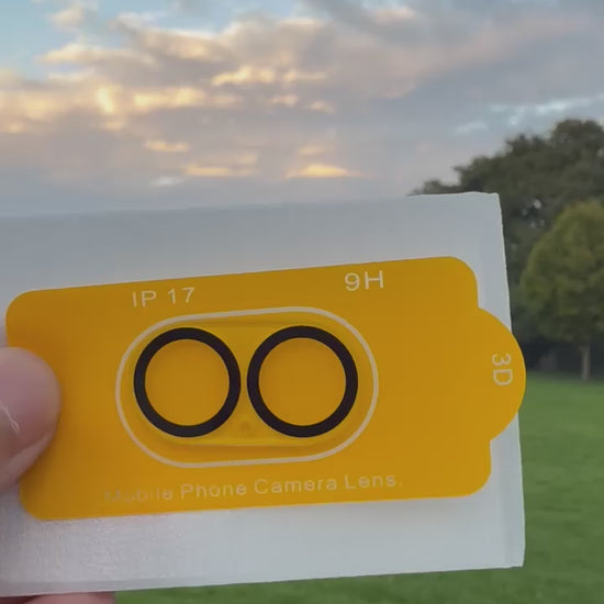 Premium Protection Kit iPhone 17 showing mobile phone camera lens cover in hand outdoors.