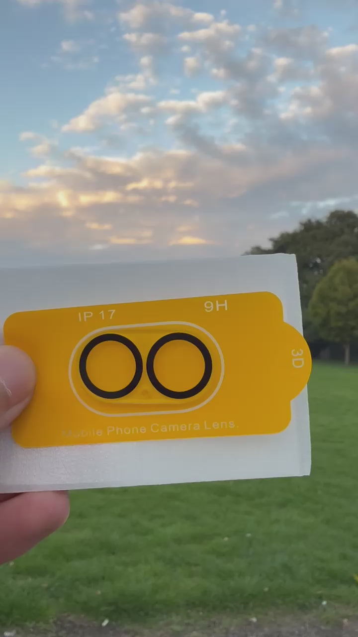 Premium Protection Kit iPhone 17 showing mobile phone camera lens cover in hand outdoors.
